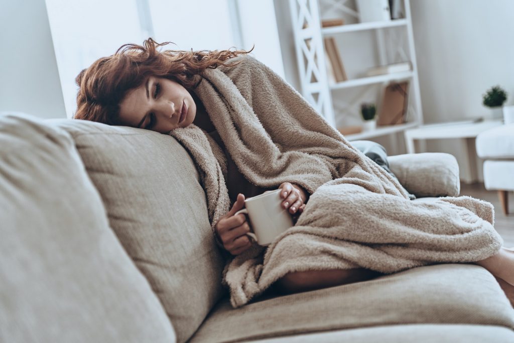 Feeling sick. Sick young women covered with blanket resting at home while sitting on the sofa